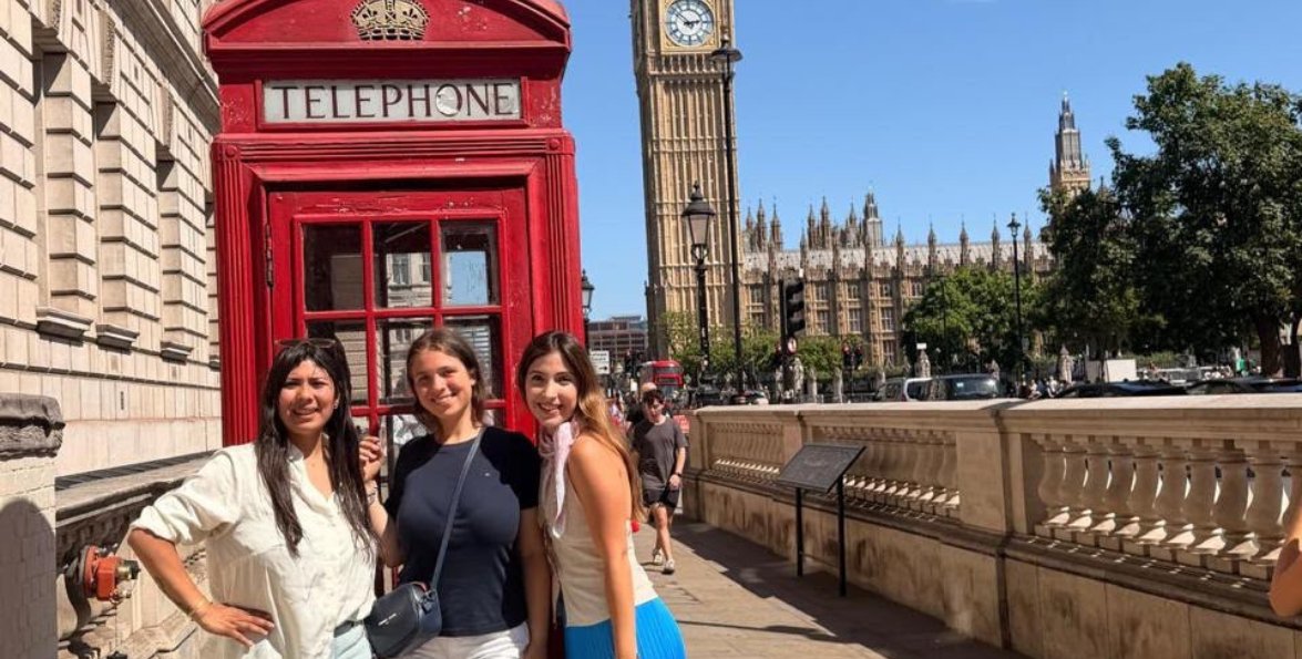Tres jóvenes posan junto a una cabina telefónica roja con el Big Ben de Londres de fondo.