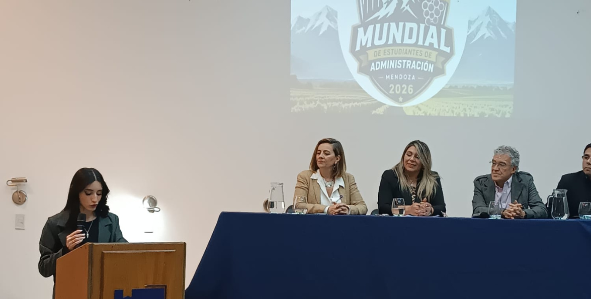 Una oradora habla desde el atril mientras el panel escucha, con el logo del Mundial de Estudiantes de Administración proyectado detrás.