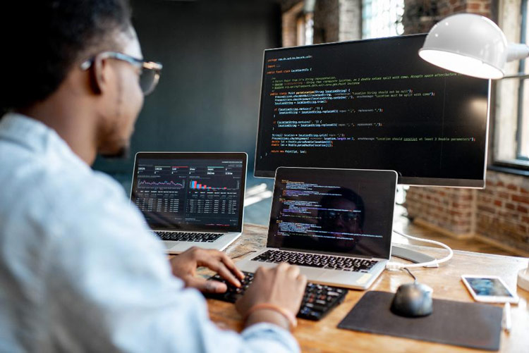 Programador frente a un monitor y dos computadoras portátiles con código en pantalla