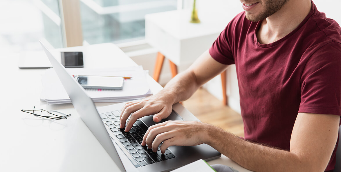 Joven que escribe en el teclado de una computadora portátil sobre un escritorio blanco