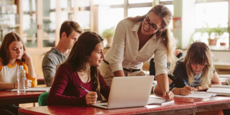 Docente que acompaña a estudiantes que trabajan con una computadora portátil en un aula
