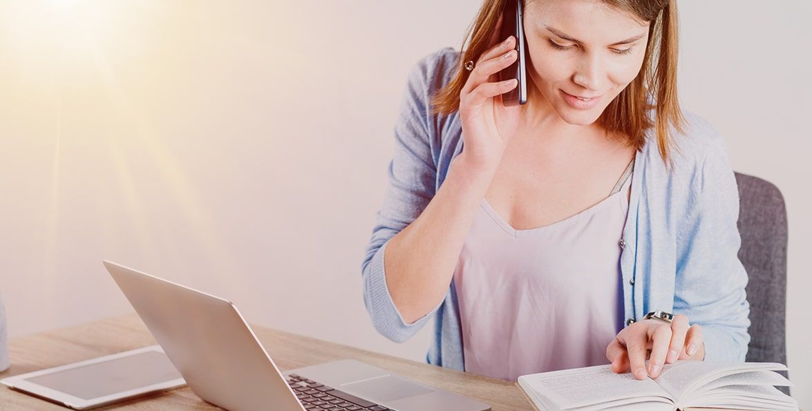 Mujer que habla por teléfono mientras toma notas en un escritorio con una computadora portátil