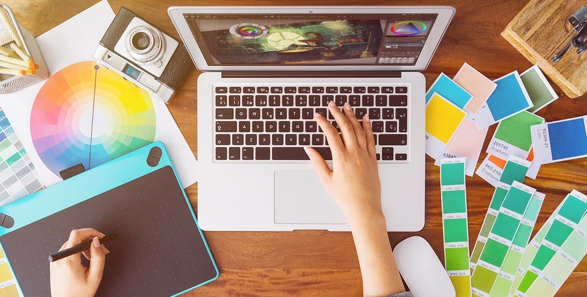 Escritorio de diseño con una computadora portátil, tableta gráfica, círculo cromático y muestrarios de color
