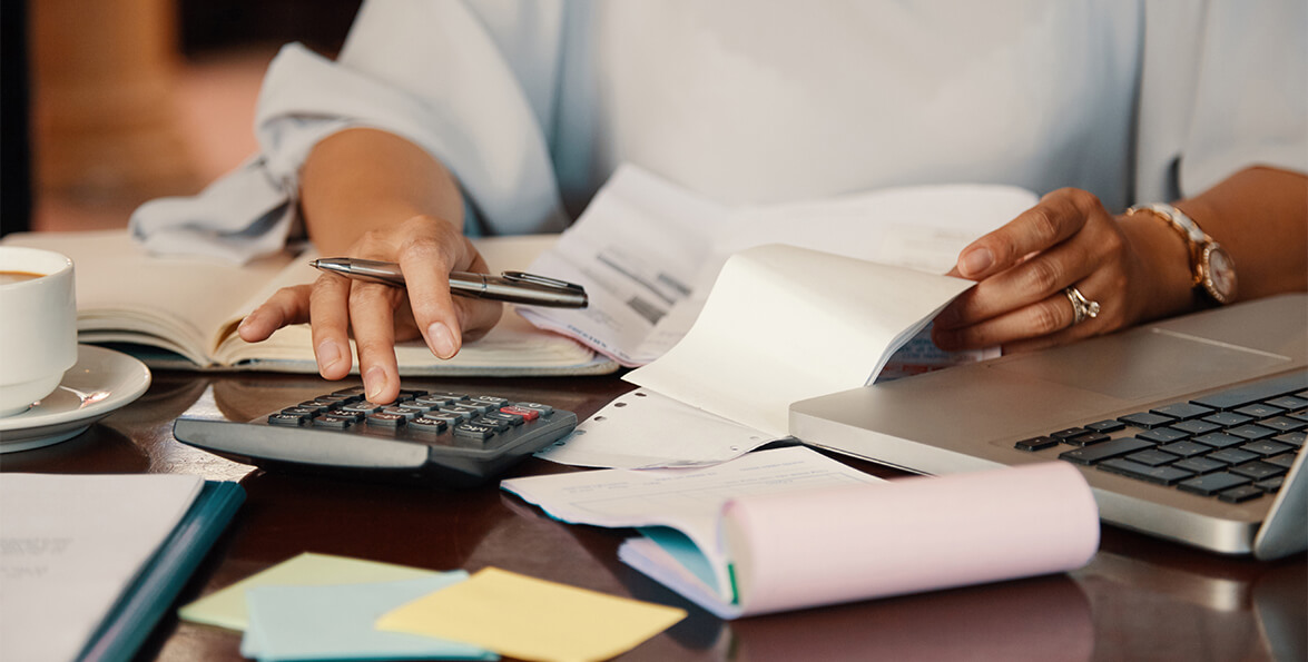 Manos que usan una calculadora junto a una computadora portátil, papeles y anotadores sobre un escritorio